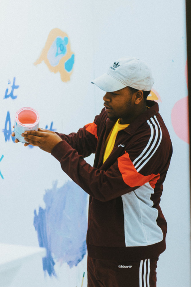 A creator holding pink paint in front of a wall of artwork